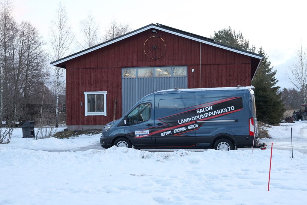 Punainen varastorakennus lumisessa maisemassa. Varaston edessä pakettiauto.