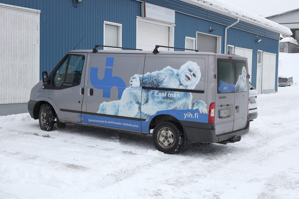 Pakettiauto sinisen rakennuksen edessä lumisessa maisemassa.