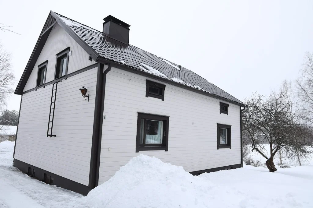 Valkoinen rintamamiestalo lumisessa maisemassa.