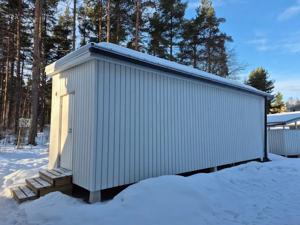 Valkoinen konttirakennus, johon maalämpöpumppu on asennettu lumisessa maisemassa.