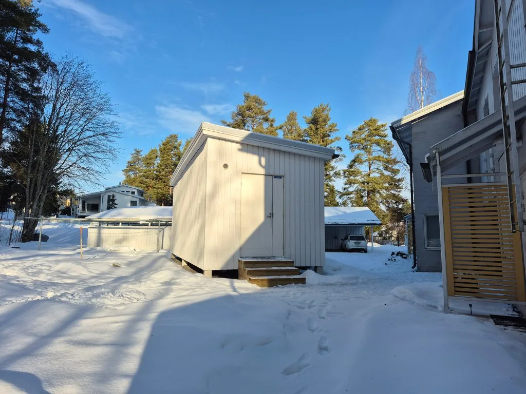Valkoinen konttirakennus, johon maalämpöpumppu on asennettu lumisessa maisemassa.