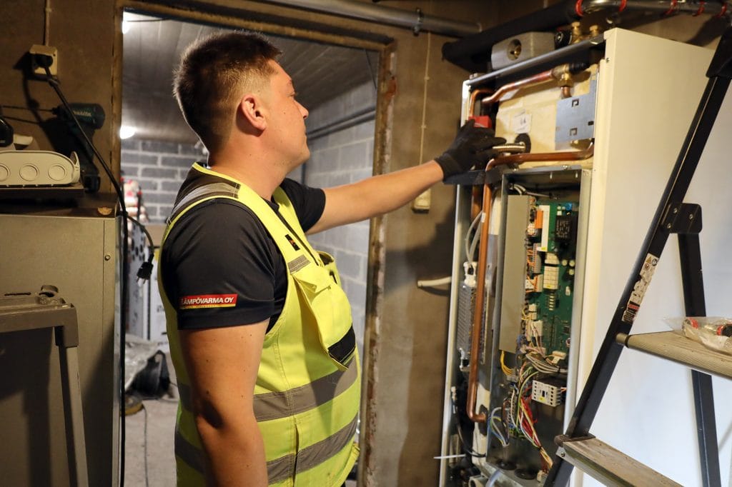Mies asentaa maalämpöpumppua teknisessä tilassa.