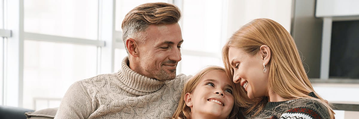 Perhe istuu sohvalla vierekkäin ja hymyilee toisilleen kuvituskuvassa.