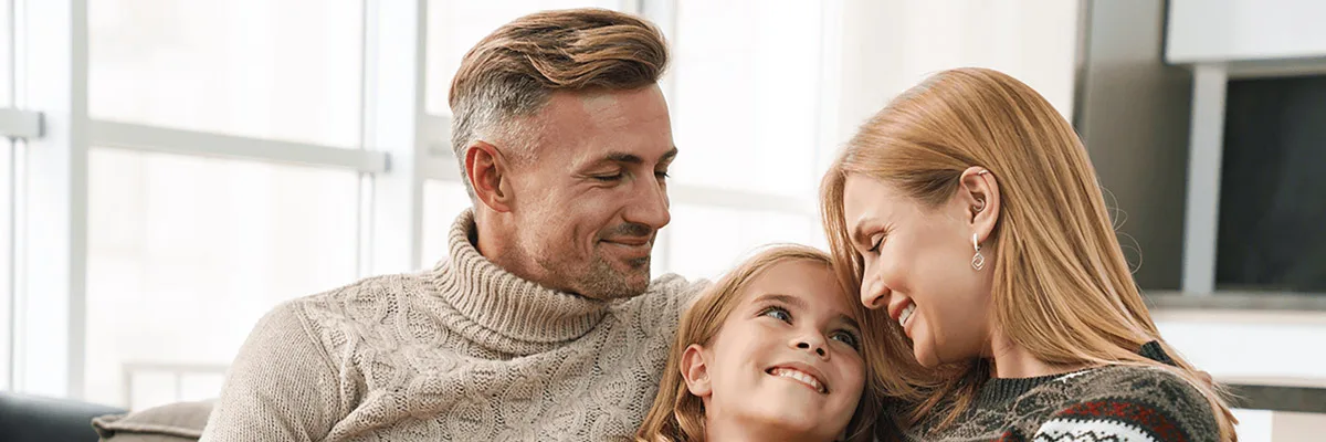 Perhe istuu sohvalla vierekkäin ja hymyilee toisilleen kuvituskuvassa.