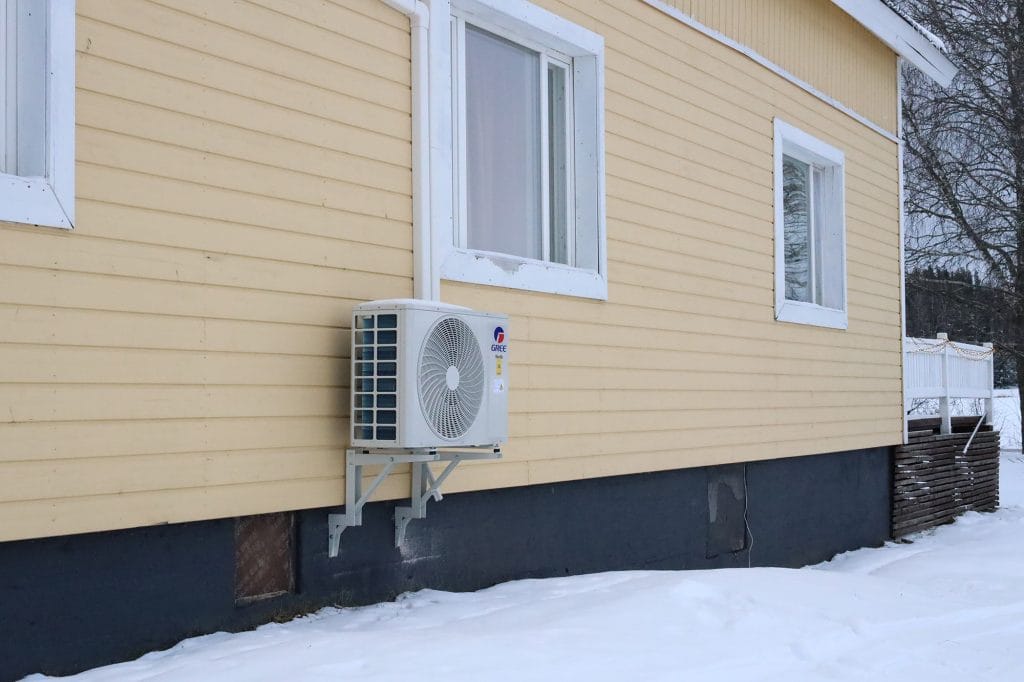 Ilmalämpöpumpun ulkoyksikkö keltaisen talon seinällä.