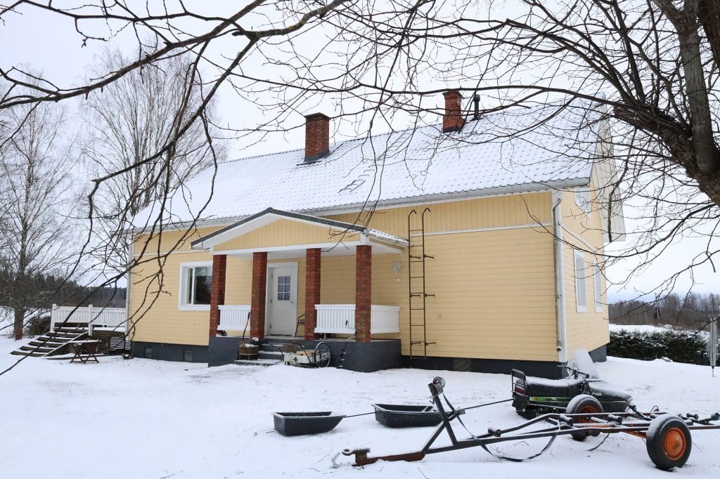 Keltainen omakotitalo lumisessa maisemassa.