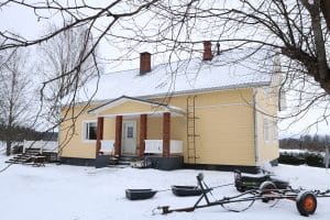 Keltainen omakotitalo lumisessa maisemassa.