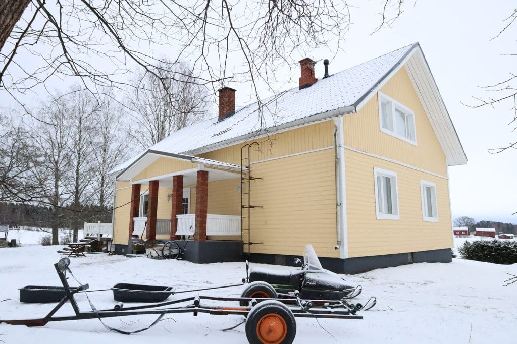 Keltainen omakotitalo lumisessa maisemassa.